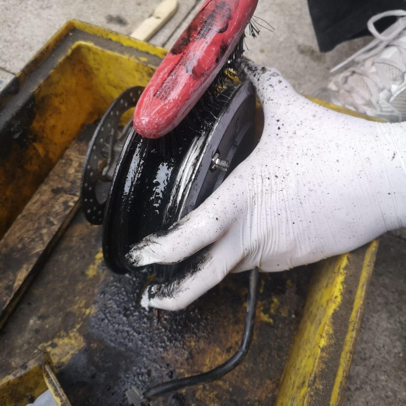 Schwarze, ölige Oberfläche eines Geräts wird mit einer Hand und einem roten Werkzeug gereinigt.